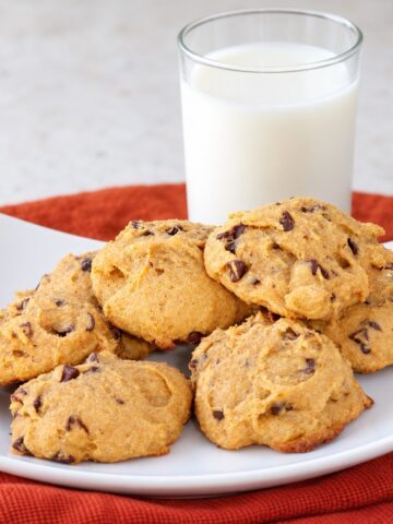 Homemade gluten-free pumpkin chocolate chip cookies on a white plate with a glass of milk.