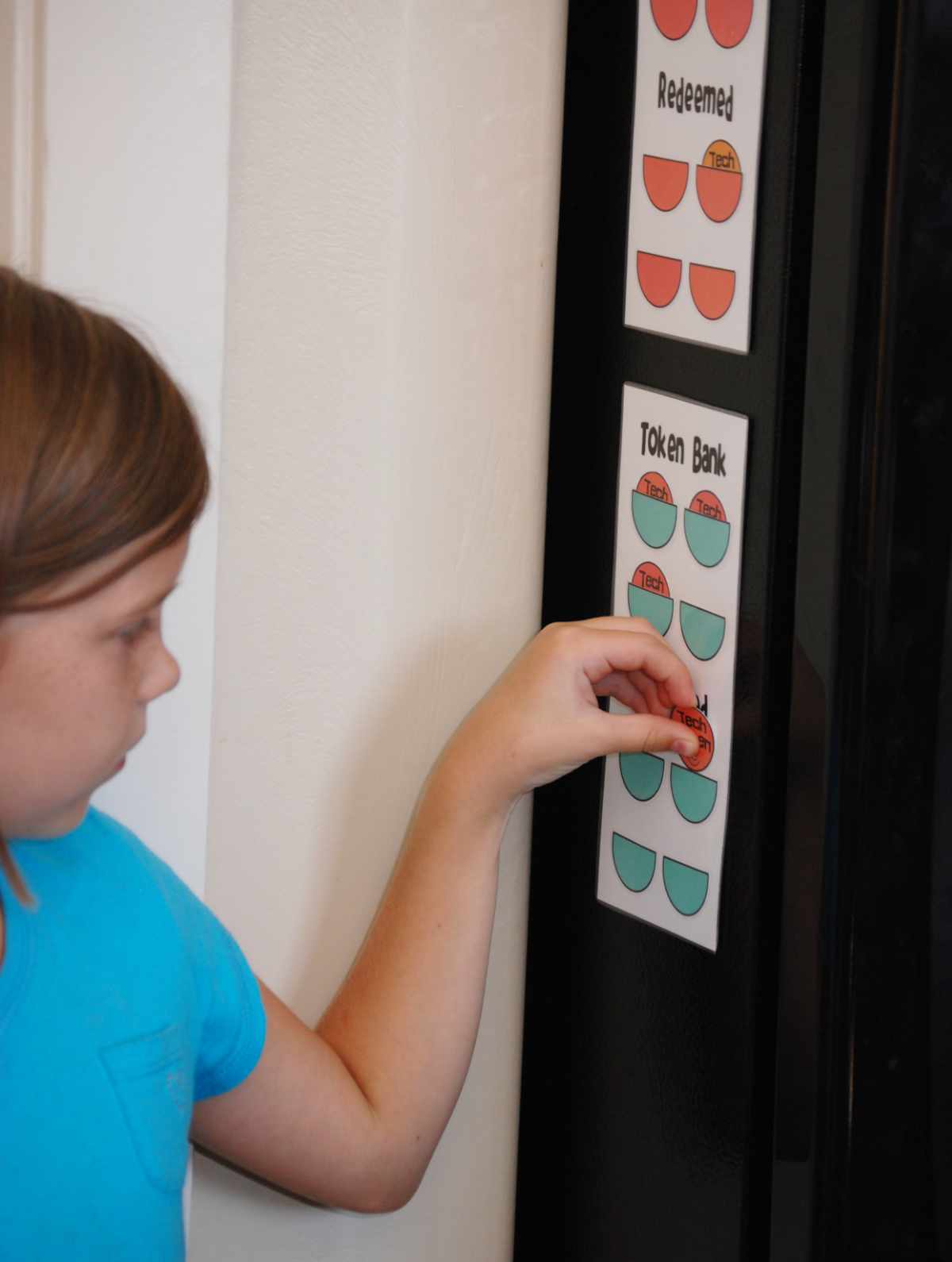 Child moving a token on a refrigerator-mounted screen time token chart.