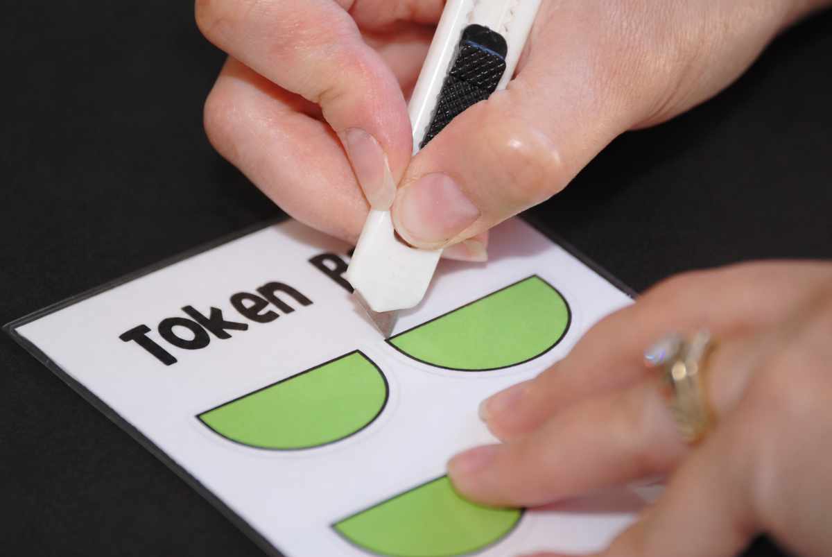 Adult using a craft knife to cut out green pockets for the screen time token system.