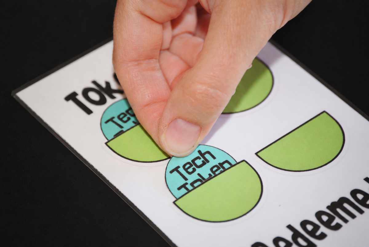 Hand placing a blue Tech Token into a finished green pocket on the screen time token chart.