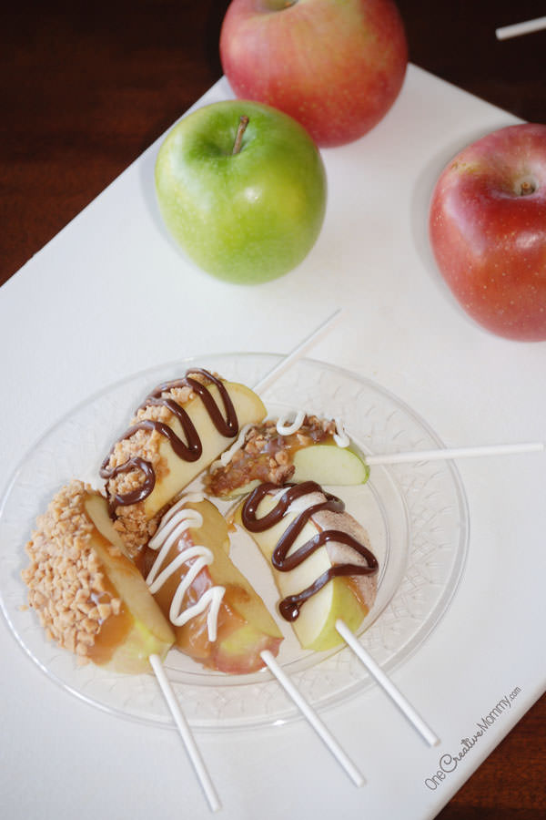 Caramel Apple Pops pack all the flavor of a caramel apple with a manageable serving size. These fancy apple slices on a stick are perfect for a tasting party or as a neighbor gift. {OneCreativeMommy.com} Caramel candy recipe included.