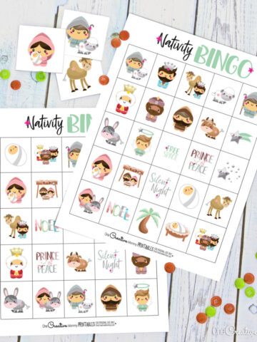 Two nativity bingo boards laying on a white tabletop. Calling cards for the game and M & M's candies are scattered across the game boards.