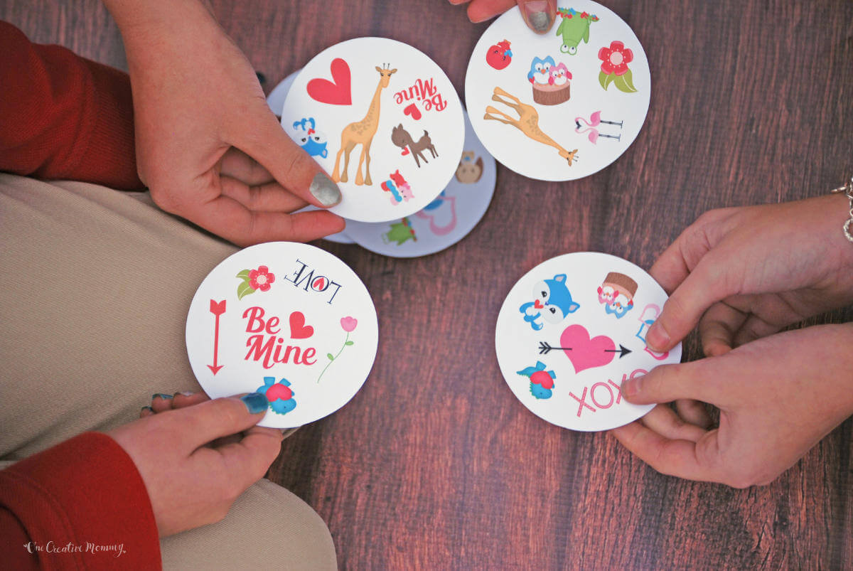 Closeup of three young girls playing Valentine's Day Spot It card game. Cards are round and contain valentine-themed images.