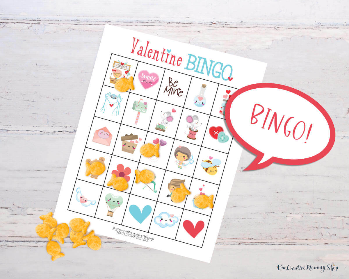 A cute Valentines Day bingo card is laid out on a white wooden table. There is a pile of Goldfish crackers on the table, and several cover spaces on the bingo card. Five spots in a row are covered, and there is a word bubble that reads, Bingo!