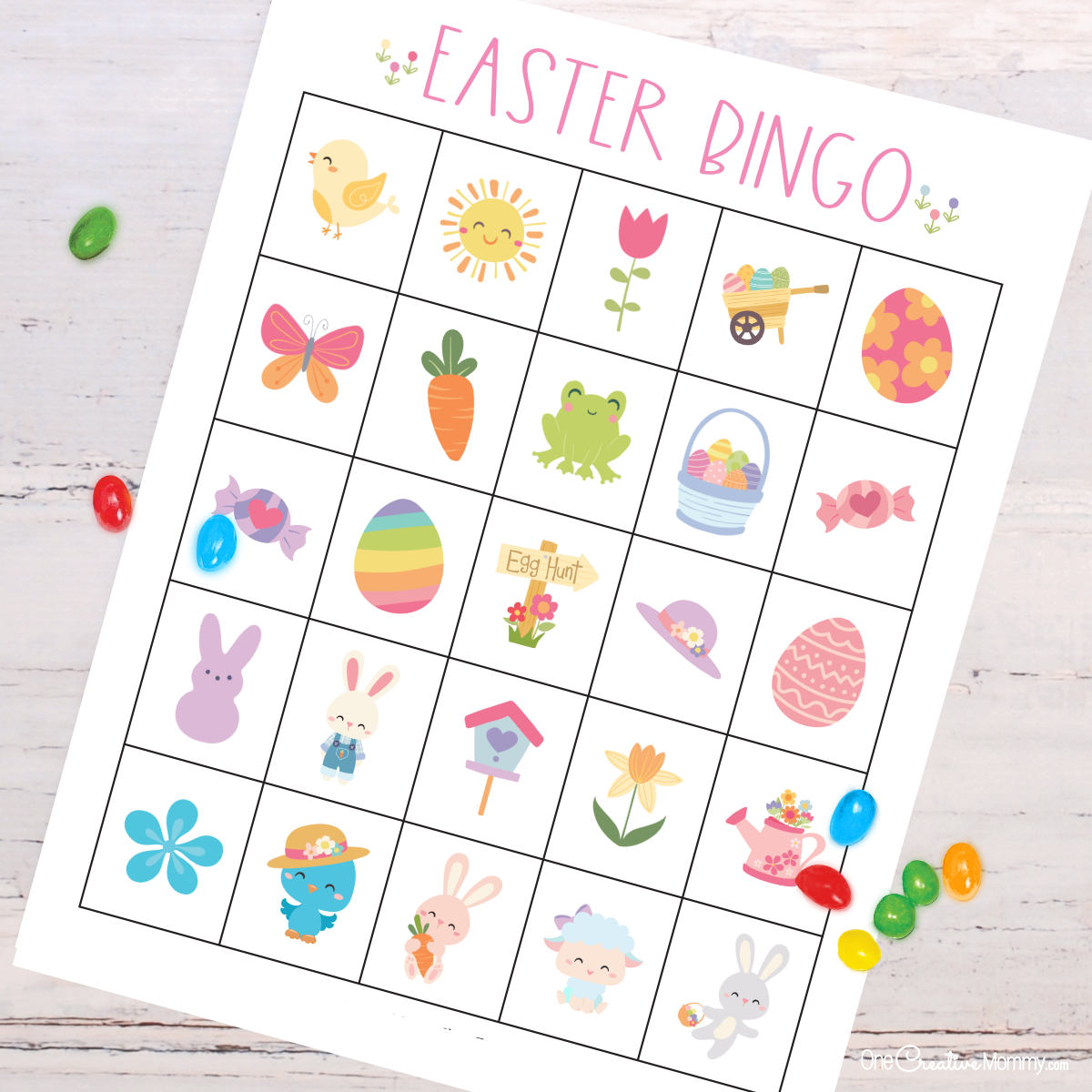 Zoomed-in view of an Easter bingo card laying on top of a white wooden table. Jellybeans are scattered across the game board. Pictures include Easter bunnies, Easter eggs, flowers, frogs, candy, baby animals, Easter baskets, butterflies, a birdhouse, and more.