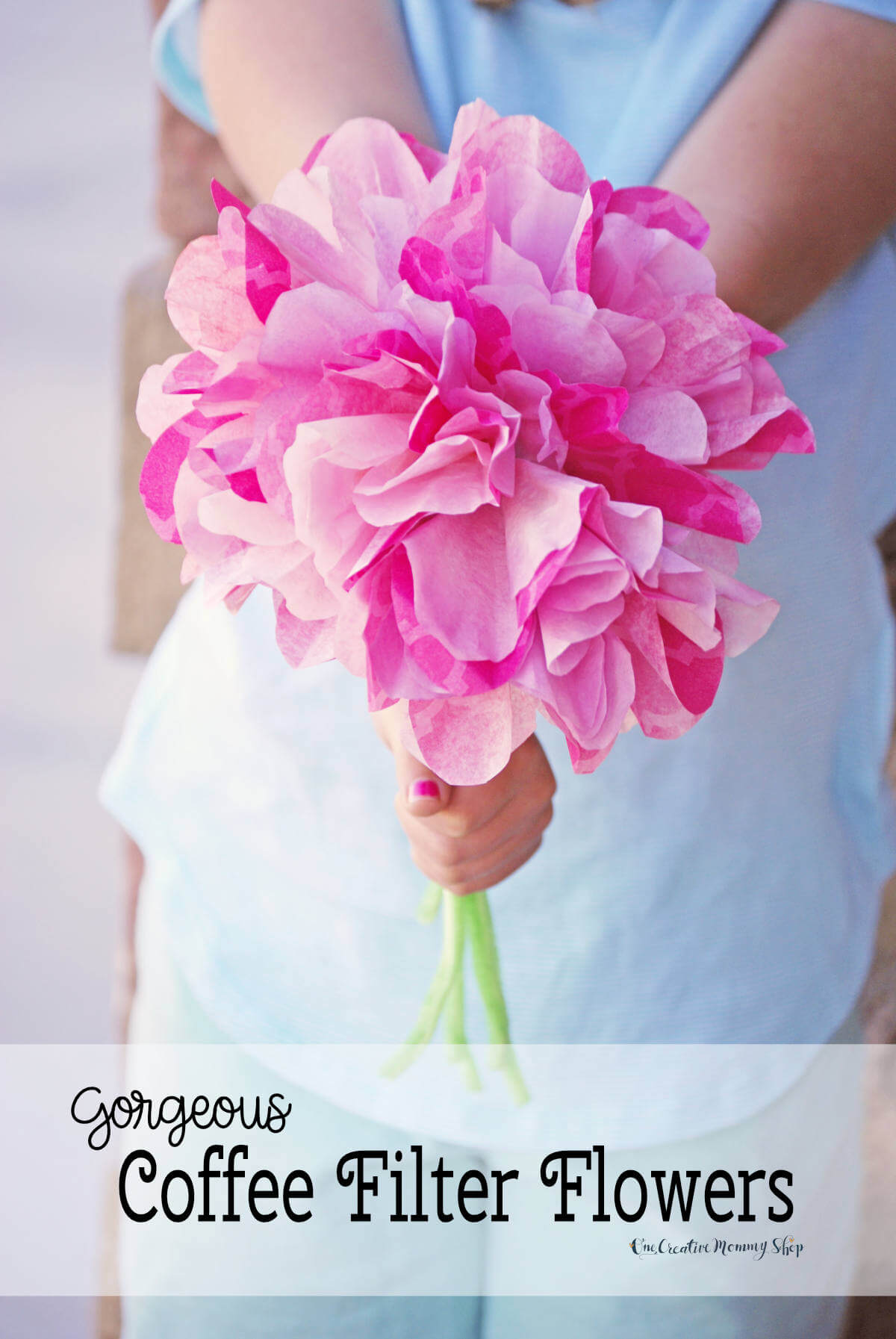 Closeup of the hands of a child holding out a bouquet of pink coffee filter flowers with green chenille stems. Text: Gorgeous Coffee Filter Flowers