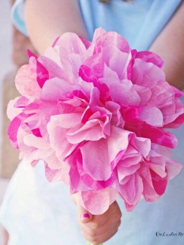 Closeup of the hands of a child holding out a bouquet of pink coffee filter flowers with green chenille stems.