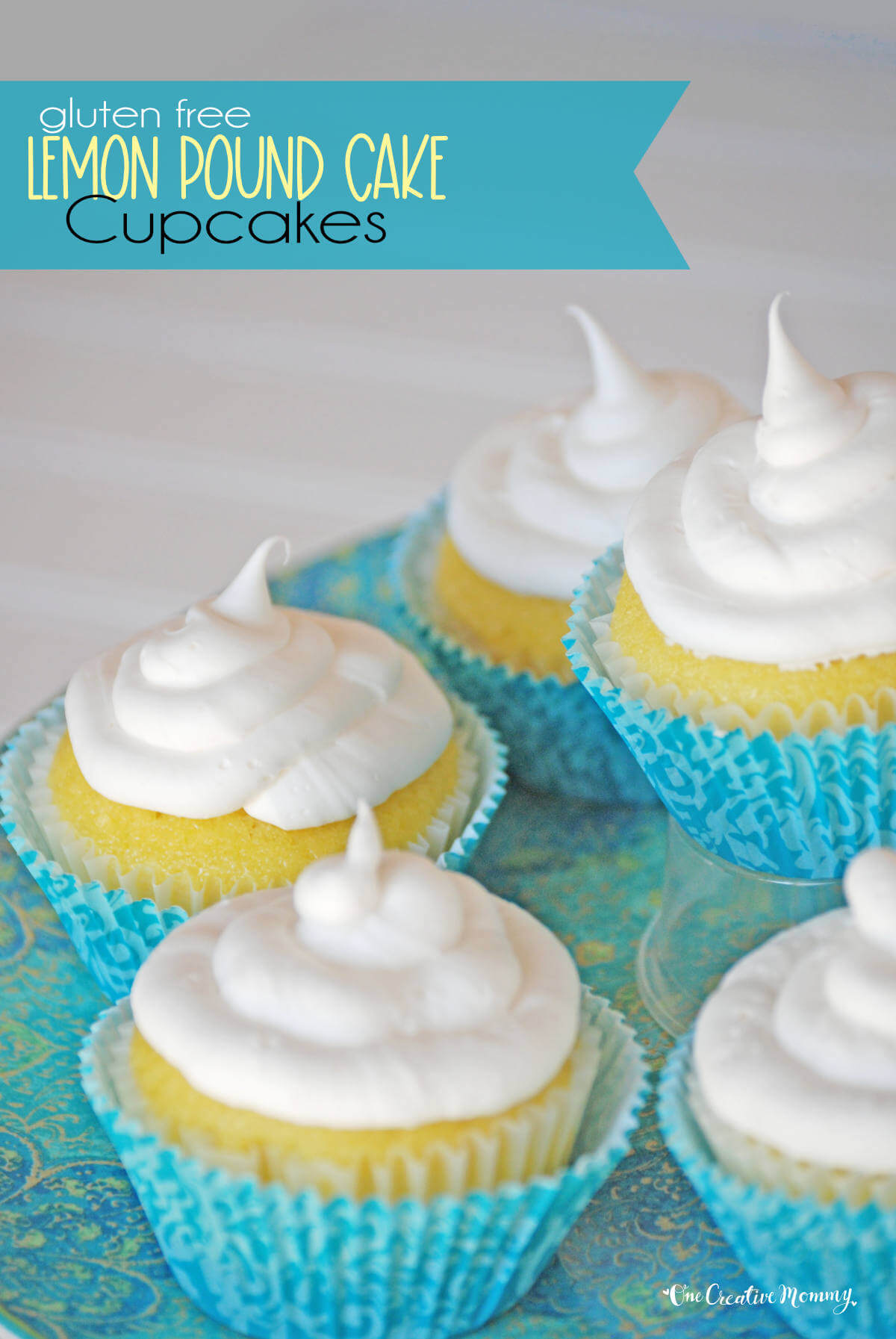 Several delicious gluten free lemon pound cake cupcakes arranged on a pretty plate. They are bright yellow, frosted with white frosting, and nestled inside blue cupcake liners.