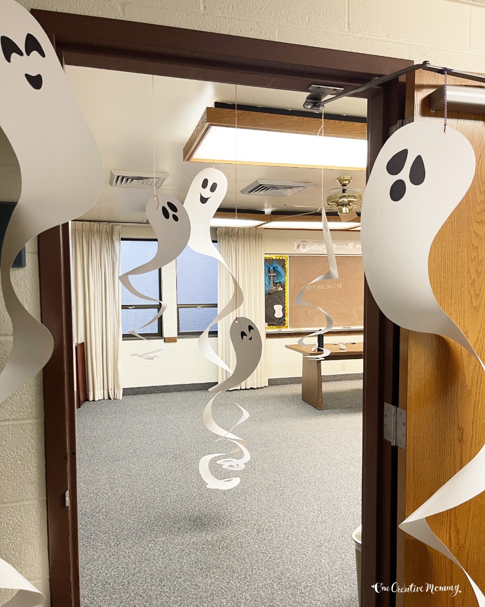 Several sprial ghosts with black eyes and mouths hang from the ceiling and dangle almost all the way to the floor. They are hanging from the ceiling and in a doorway of a classroom.