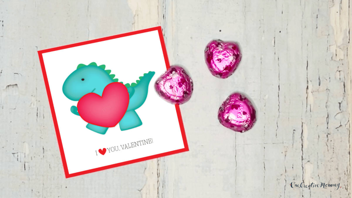 A square-shaped card with a cute dinosaur holding a giant red heart if shown with a few Valentine's Day Dove chocolate hearts. The card says, I heart you Valentine!