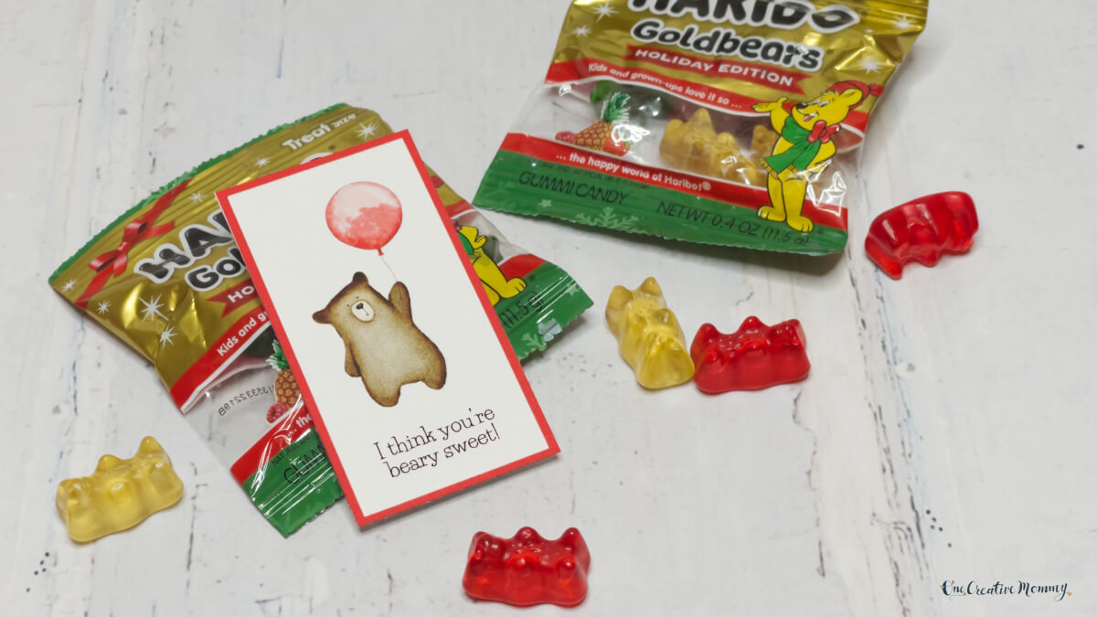 Two small packages of gummy bears are shown with several gummy bears scattered across the table. A Valentine's Day card is attached to the bag that says, I think you're beary sweet! There is a picture of a cute bear holding a red balloon on the tag.