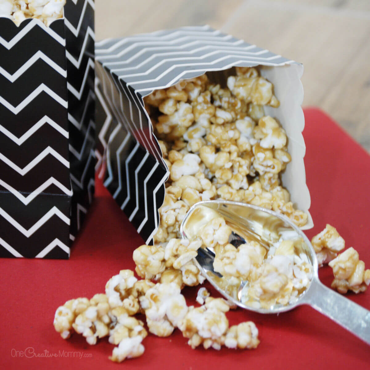 Salted Caramel popcorn spills out of an overturned black and white chevron-patterned popcorn bag onto a red table.