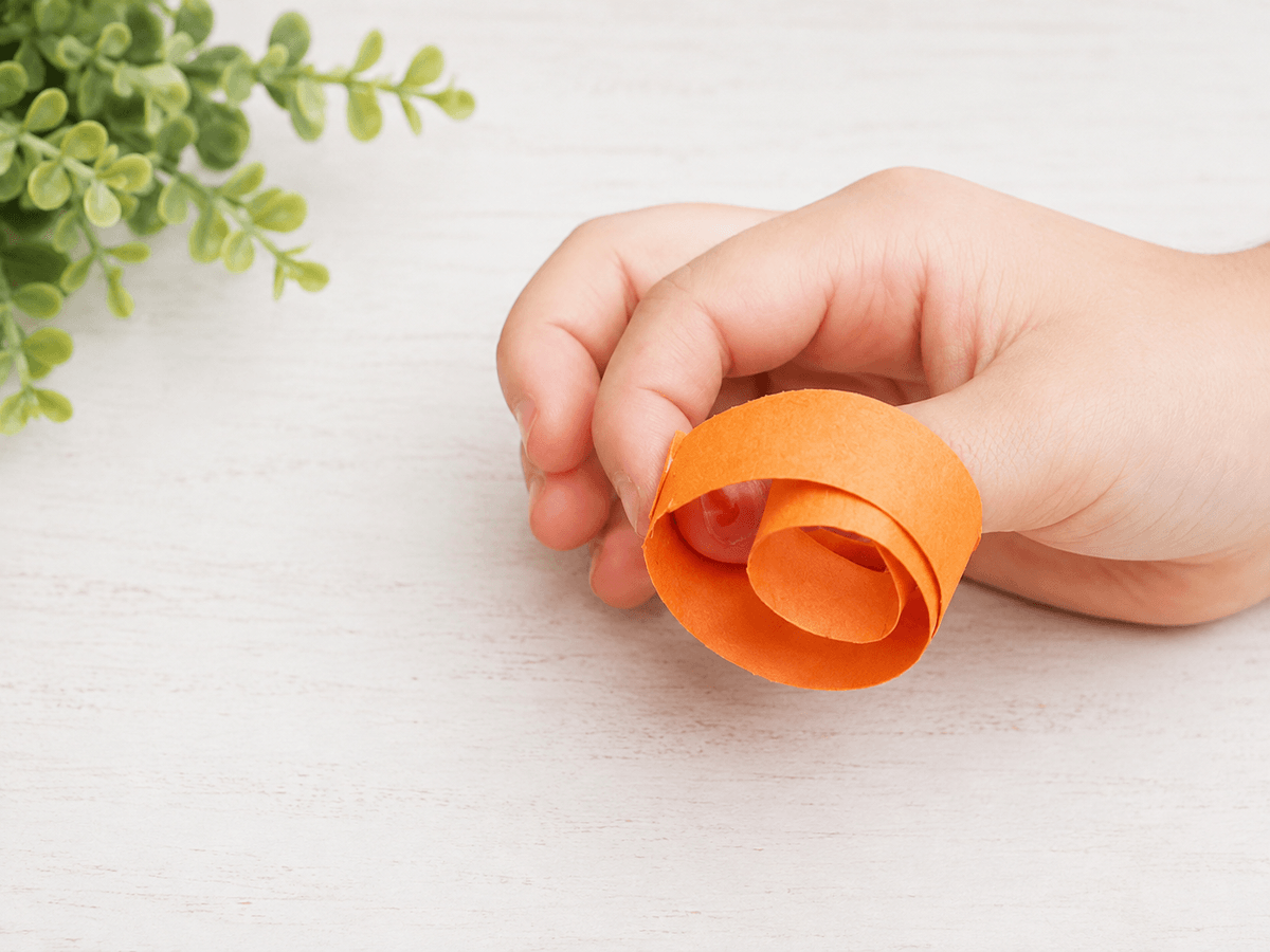 Hand rolling an orange paper strip into a circle