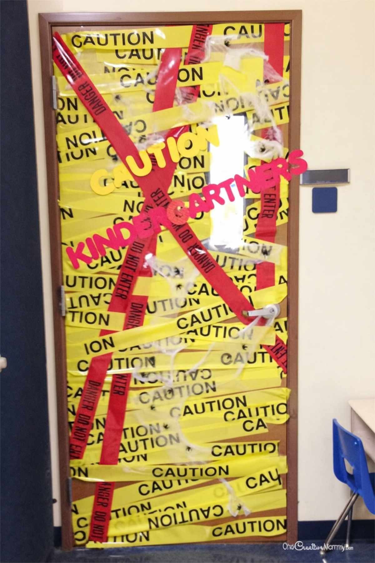 Halloween classroom door covered with yellow caution tape, red danger tape, and spiderwebs