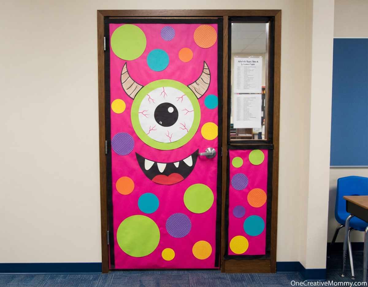 Pink Halloween door decorated as a one-eyed monster with gray horns, polka dots, and a silly toothy smile.
