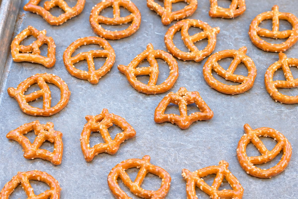 Halloween bat and jack-shaped pretzels arranged on a baking sheet for homemade Rolo pretzel treats.