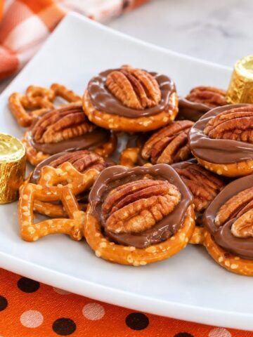 Halloween Rolo pretzel treats with melted chocolate and pecans on a white plate.