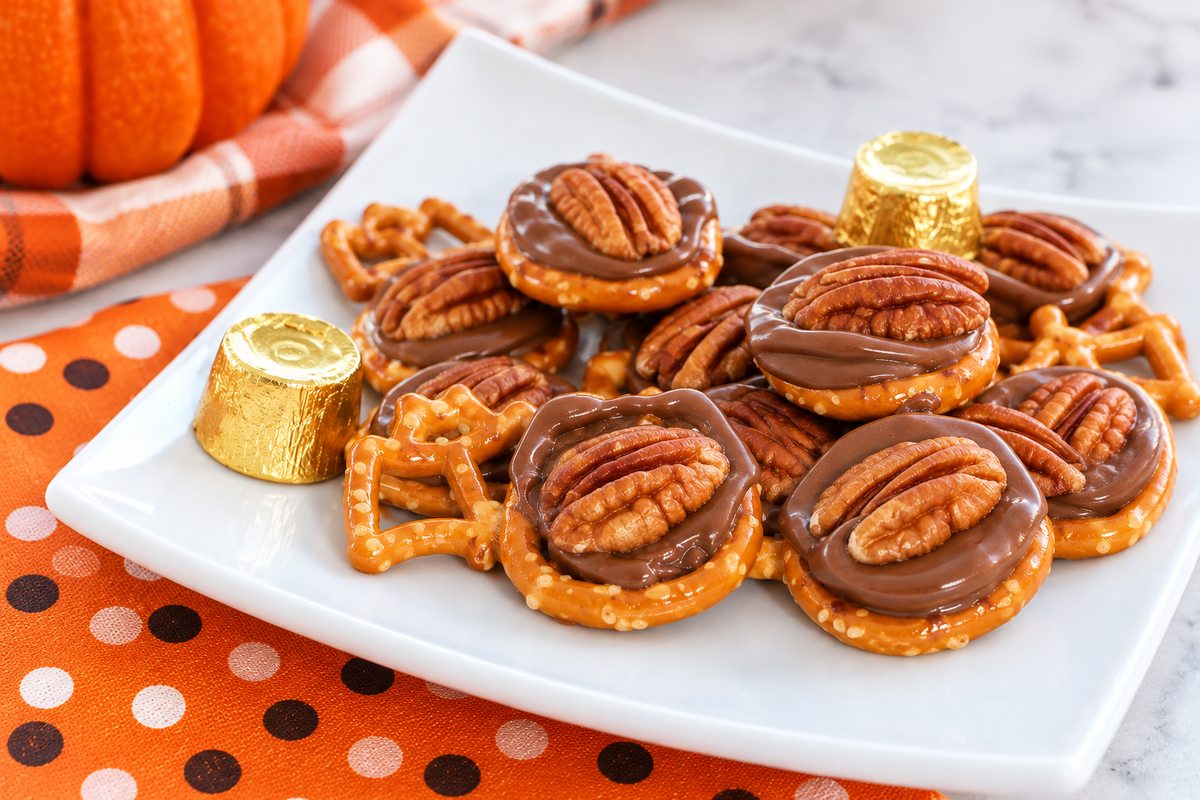 Finished Halloween Rolo pretzel treats topped with melted chocolate and pecans on a white plate with fall decorations.