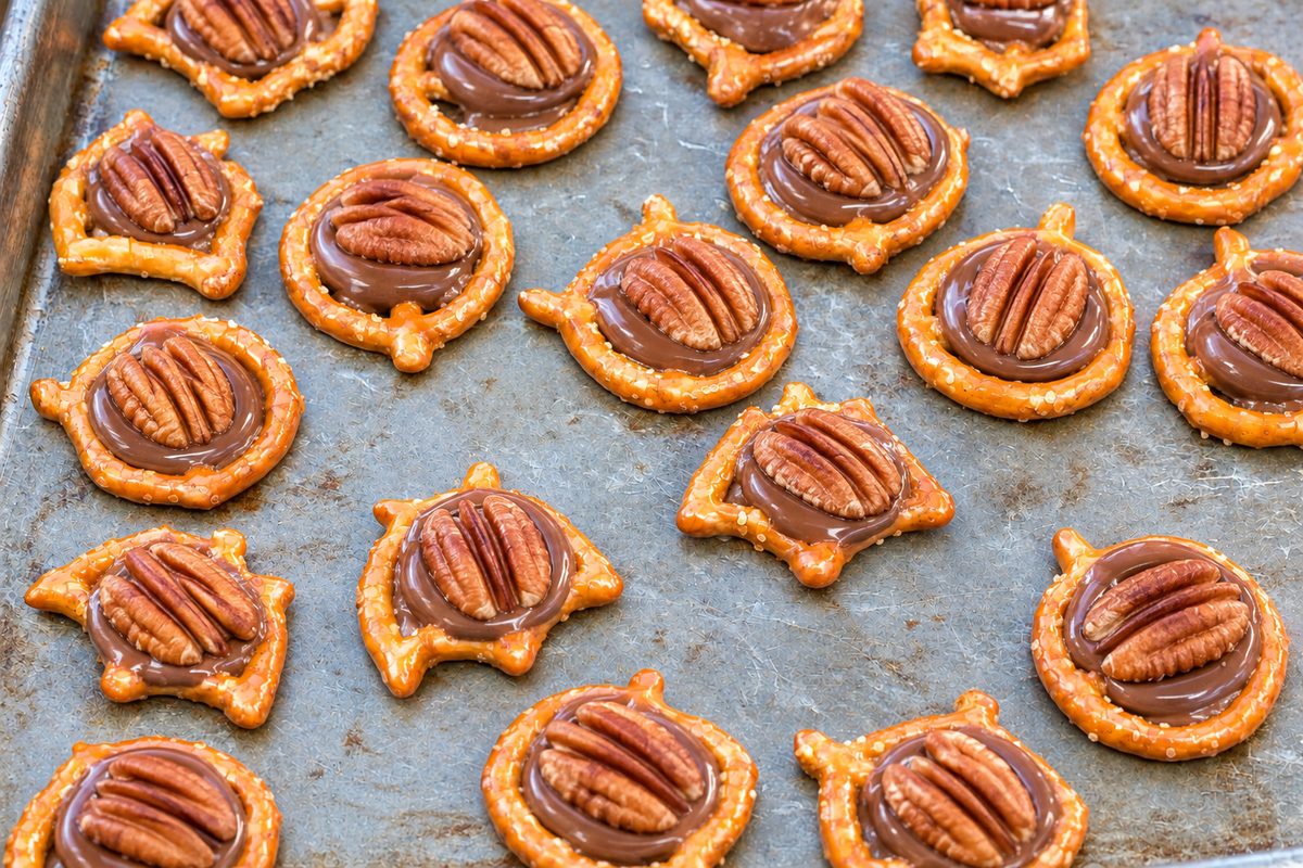 Halloween bat and jack-shaped pretzels topped with melted Rolo chocolate and pecan halves on a baking sheet.